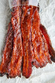 bacon strips sitting on top of a piece of wax paper next to a glass container