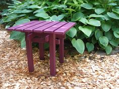 a small purple bench sitting in the middle of some wood chips next to a bush