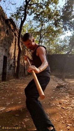 a man holding a baseball bat on top of a dirt field next to a building