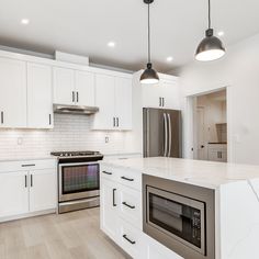 a large kitchen with white cabinets and stainless steel appliances, along with an island in the middle