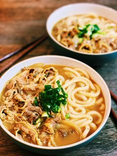 two bowls filled with noodles and meats next to chopsticks on a table