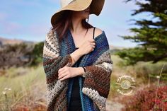 a woman wearing a crocheted shawl standing in a field with her hat on