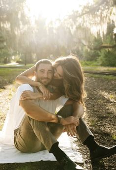 a man and woman are sitting on a blanket in the grass, hugging each other