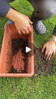 a person kneeling down to scoop dirt into a container on the grass with their hands