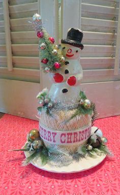 a snowman is sitting on top of a christmas cake with ornaments around it and the words merry christmas