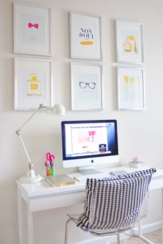 a white desk topped with a computer monitor next to a wall covered in framed pictures