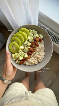 a person holding a bowl of oatmeal with sliced kiwi and almonds