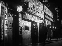 an old time movie theater at night with people standing outside the doors and looking in