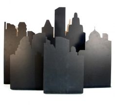 three pieces of black paper with buildings in the background and one piece cut out to look like skyscrapers