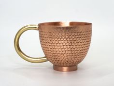 a copper colored cup with a handle on a white background, it looks like the inside of a fish scale pattern