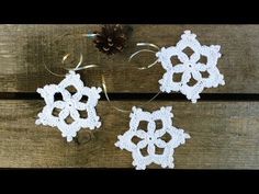 three crocheted snowflakes sitting on top of a wooden table next to a pine cone