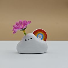 a small white cloud with a pink flower sticking out of it's side and a rainbow in the background