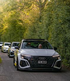 two men driving an audi car on a road with other cars in the back ground