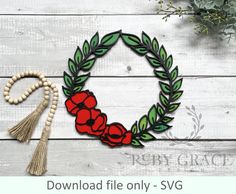 a wreath with flowers and tassels hanging on a white wooden wall next to a beaded necklace