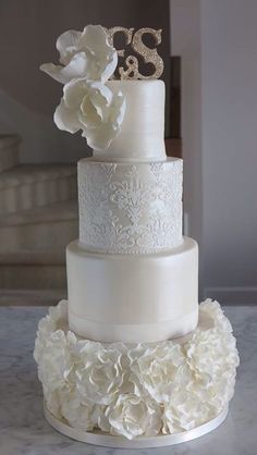 a three tiered wedding cake with white flowers on the bottom and two initials on top