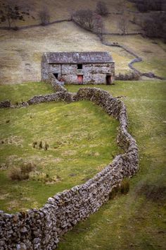 an old stone building in the middle of a field with a rock wall around it