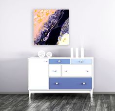 an abstract painting hangs on the wall next to a white and blue dresser with drawers