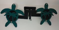 two green turtle shaped key chains hanging from a hook on a white wall next to a clipboard