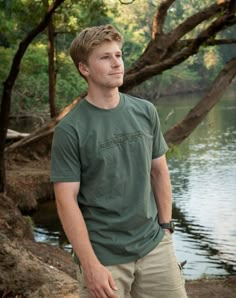 a man standing in front of a body of water wearing a green shirt and khaki pants