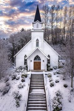 a white church with stairs leading up to it and trees in the background covered in snow