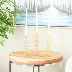 three candles sitting on top of a table next to a potted plant and painting