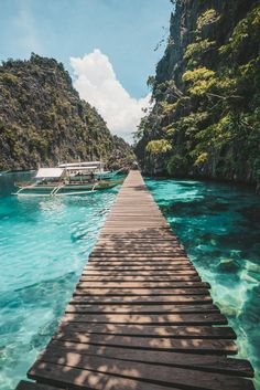 a long wooden dock leading to boats in the water