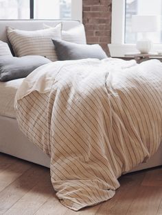 an unmade bed with pillows and blankets on it in a room next to a brick wall