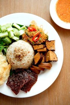 a white plate topped with lots of food next to a bowl of soup and sauce