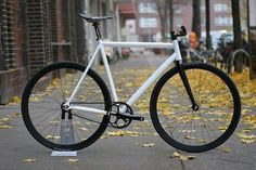 a white bike parked on the side of a street next to trees with yellow leaves