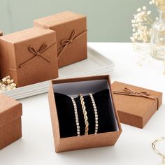 four boxes with bracelets and necklaces in them on a table next to flowers