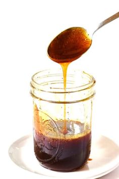 a spoon is pouring sauce into a glass jar on a plate with a white background