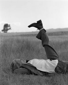 a woman laying on her back in the middle of a field with a shoe hanging over her head