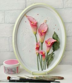 a white plate with pink flowers on it next to paintbrushes and some brushes