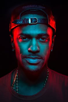 a man wearing a baseball cap and beaded necklace in front of a black background