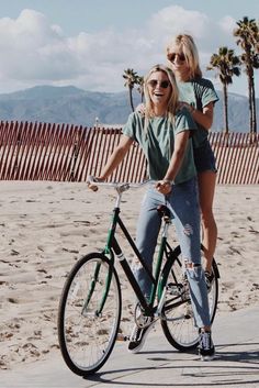 two women riding bikes on the beach with palm trees in the background