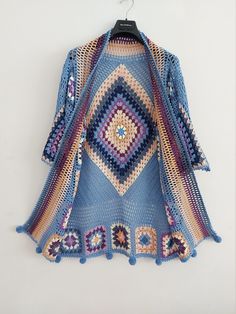 a blue crocheted sweater hanging on a white wall next to a black hanger