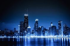 the city skyline is lit up at night with lights reflecting in the water and skyscrapers