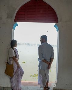 a man and woman standing in front of an open door looking out at the water