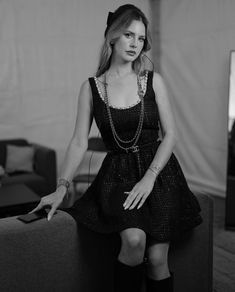 a woman sitting on top of a couch in a black dress and high heel boots