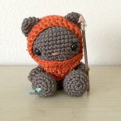 a crocheted teddy bear with an orange scarf holding a stick