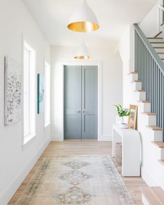 a white hallway with stairs and rugs on the floor, next to a blue door