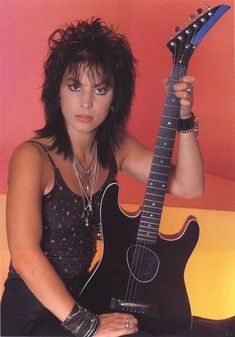 a woman holding an electric guitar in her right hand and posing for the camera,