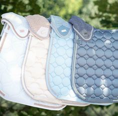 four different colored saddle pads hanging from a line