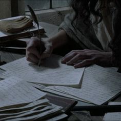 a person writing on paper with a pen in their hand while sitting at a table full of papers