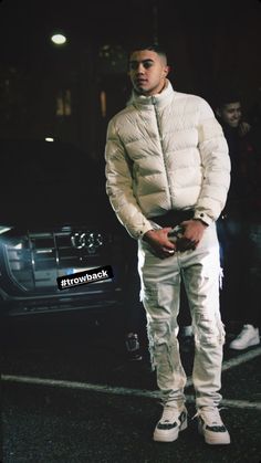 a man standing in front of a car wearing white pants and a puffy jacket