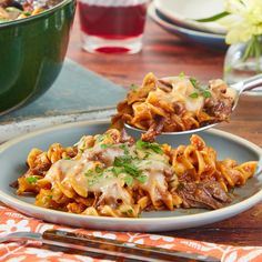 two spoons full of pasta and meat on a plate with other dishes in the background