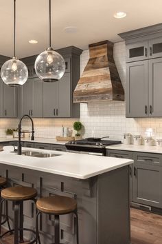 a kitchen with gray cabinets and white counter tops, two pendant lights over the island