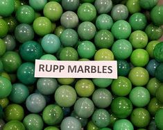 a pile of green and brown balls with a sign that reads rupp marbles