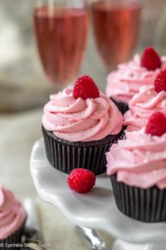 cupcakes with pink frosting and raspberries sit on a white plate