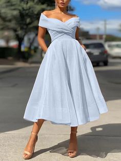 a woman in a blue dress is standing on the sidewalk and looking at the camera